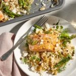 Ein Teller mit gebratenem Lachs, Reis, Spargel und frischen Kräutern, serviert mit einer Gabel. Gesundes und schmackhaftes Gericht.